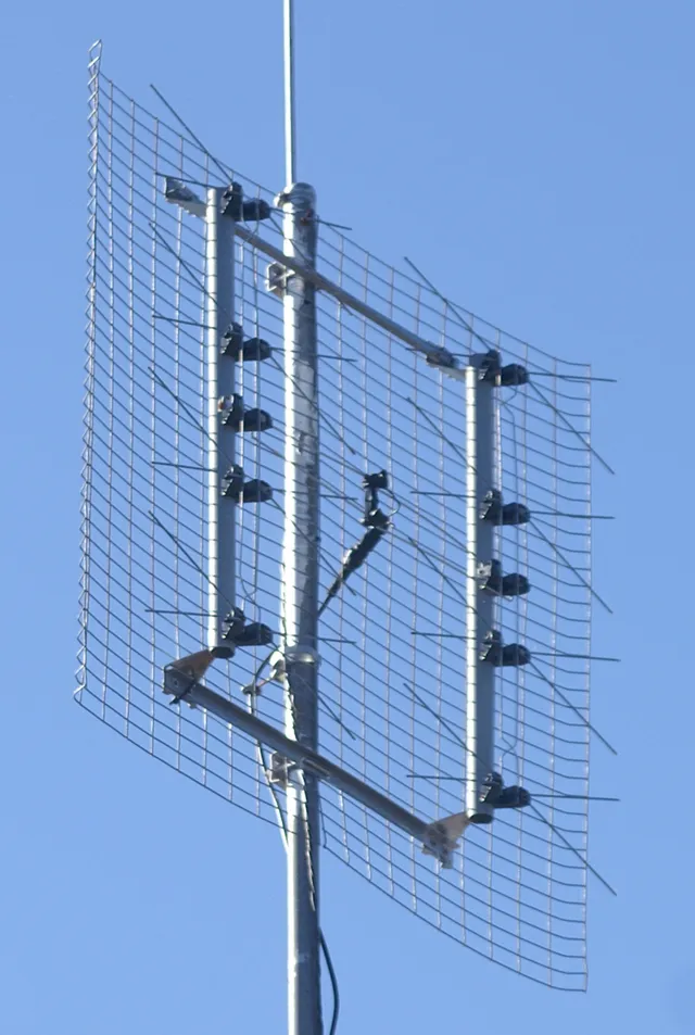 Antena UHF de tipo panel plano (grilla con elementos en forma de moño) montada sobre un mástil, contra el cielo